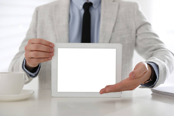 Businessman holding modern tablet with blank screen at white table in office, closeup - Foto, Imagem