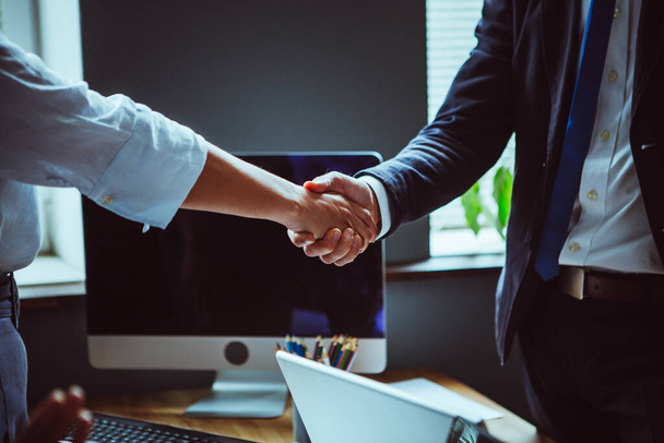 Businessman and businesswoman shake hands after team brainstorming. Close up shot of male and female hands against of office interior with computer on the table. Business handshake concept - Photo, image