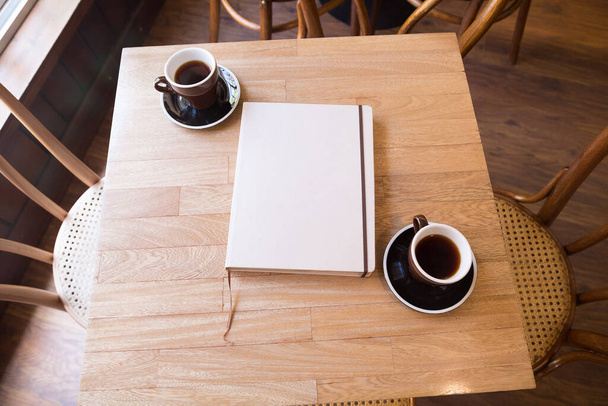 Un livre avec une couverture vide et deux cafés noirs sur la table, vu d'en haut
 - Photo, image