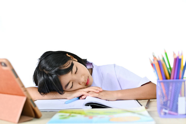 Iskolás lány egyenruhában ül Alszik az asztalon közelében tabletta és könyv, koncepció a hajlás vagy vizsga az online e-learning tanár és álmosság vagy tanulmány kemény. - Fotó, kép