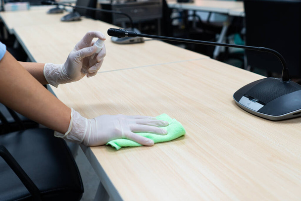 worker hand wearing gloves using disinfectant spray and cloth to clean microphone in conference room to prevent covid-19 or coronavirus infection. new normal and social distancing concept - Foto, afbeelding