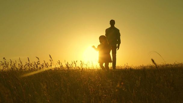 Happy healthy child with dad walk at sunset in field. Dad hugs daughter, baby plays, runs away. Silhouette of a family walking in sun. dad and baby in park. concept of a happy family. Family lifestyle - Photo, Image