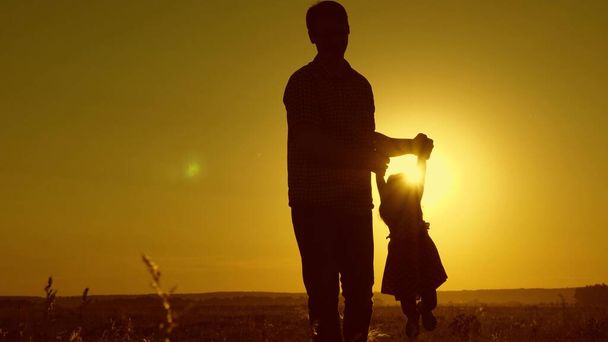 healthy father and little daughter whirl in dance at sunset. concept of happy childhood. Dad is dancing with child in her arms. happy child plays with his father at sunset. happy free family concept - Photo, Image