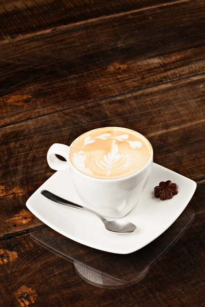 Prachtig versierde kop koffie latte en chocolade hart tegen gepolijst tafelblad - Foto, afbeelding