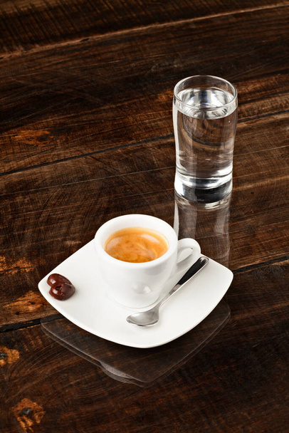 small espresso cup and a glass of water against polished table top - 写真・画像