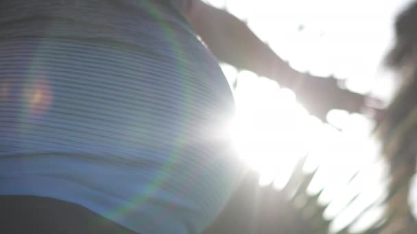 Мечтательная беременная женщина касается пальмы на морском курорте на закате  - Кадры, видео