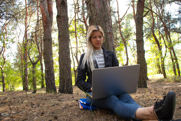 Chica ucraniana se sienta con un ordenador portátil en un bosque de coníferas cuarentena
 - Foto, Imagen