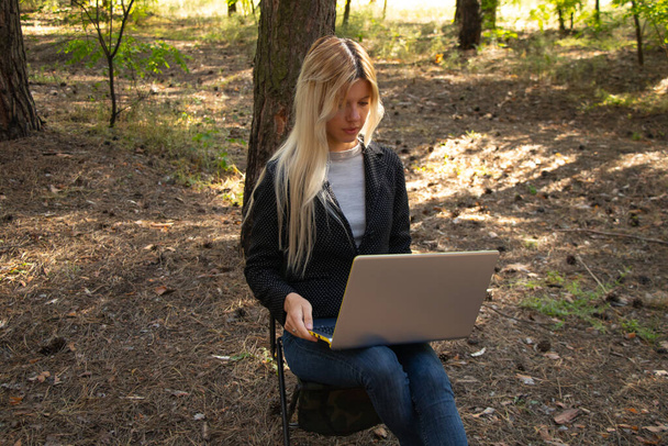 Ukrainian girl sits with a laptop in a quarantine coniferous forest - Foto, imagen