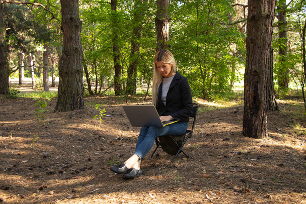 Ukrainian girl sits with a laptop in a quarantine coniferous forest - Zdjęcie, obraz