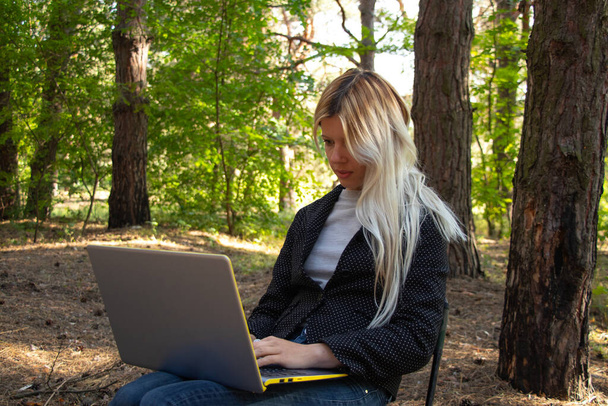 Ukrainian girl sits with a laptop in a quarantine coniferous forest - Photo, Image