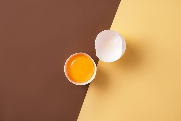 a fresh egg broken into two halves on a yellow and  brown background. Top view and copy space. Concept image - Fotoğraf, Görsel