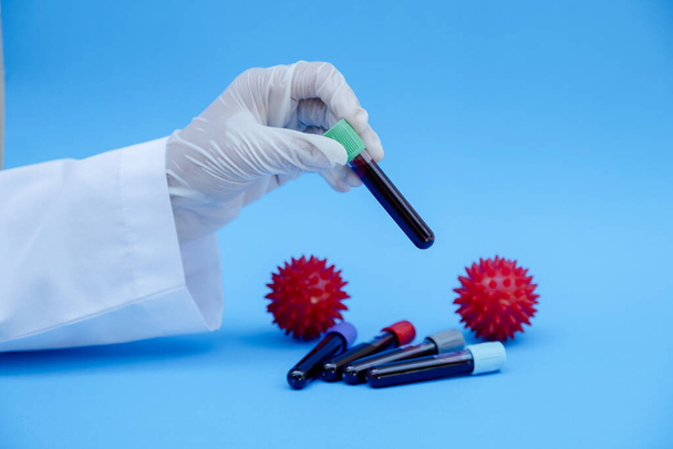 La mano del personal del laboratorio sostiene el tubo de sangre sobre fondo azul
. - Foto, Imagen