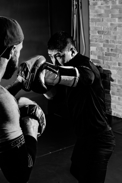 Az izmos bokszoló betölti az ütéseket az edzővel a mancsán. - Fotó, kép
