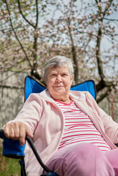 Πλάγια βολή στο κεφάλι. Ηρεμία μεσήλικη γυναίκα που κάθεται μόνη της στην καρέκλα του κάμπινγκ. Ήσυχη ώριμη γιαγιά ονειρεύεται χαλαρωτικούς διαλογιζόμενους εξερευνητές. Καλή συνταξιοδότηση. - Φωτογραφία, εικόνα