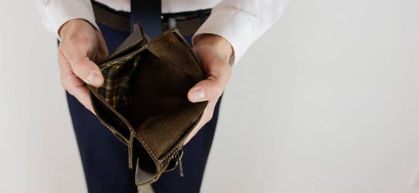 Ένας άντρας με κοστούμι κρατά στα χέρια του ένα άδειο πορτοφόλι χωρίς χρήματα. Οικονομική κρίση. Πτώχευση στις επιχειρήσεις. Ο εργοδότης είναι απογοητευμένος.. - Φωτογραφία, εικόνα