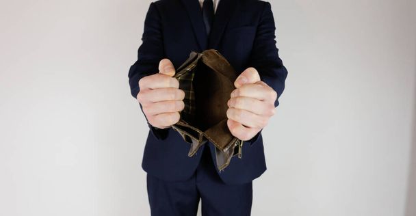 Een man in een zakenpak heeft een lege portemonnee in zijn handen zonder geld. Financiële crisis. Faillissement in zaken. De werkgever is teleurgesteld. - Foto, afbeelding