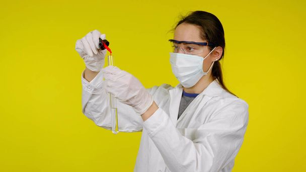 Donna in cappotto medico, maschera protettiva e occhiali gocciola reagente in provetta - Foto, immagini