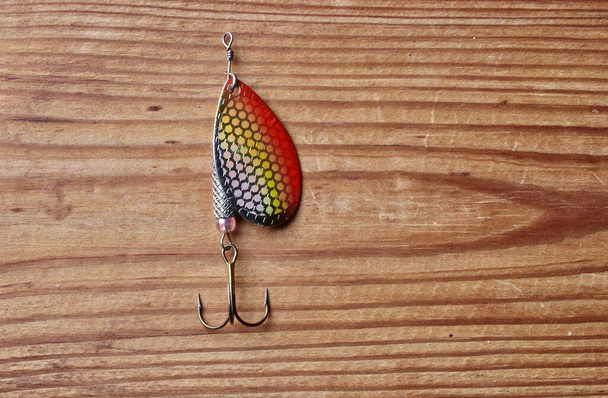 Fishing lure, bait spoon, recreation sport equipment isolated on wooden background - Photo, Image