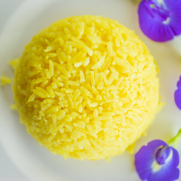 Művészet és ízletes kurkuma rizs pillangó borsóvirág fehér tányéron, ízletes sárga párolt rizs lila virágokkal fehér tányéron. Lapos fekvés. Első látásra. Közelkép. - Fotó, kép