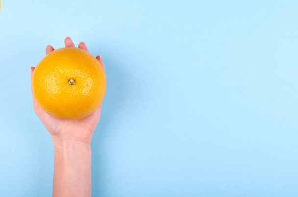 Hand with ripe and fresh orange fruit on blue background. Flat lay, overhead view image. - 写真・画像