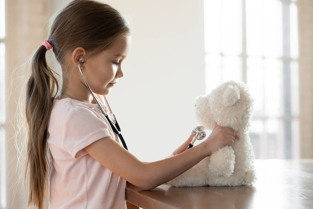 Klein meisje spelen arts spel met pluche speelgoed thuis - Foto, afbeelding