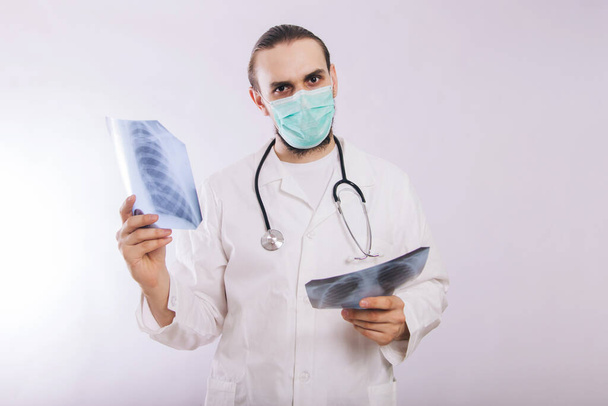 Egy fehér köpenyes orvos és egy orvosi maszk tartja a kezében a képeket a tüdő röntgen fehér alapon. - Fotó, kép