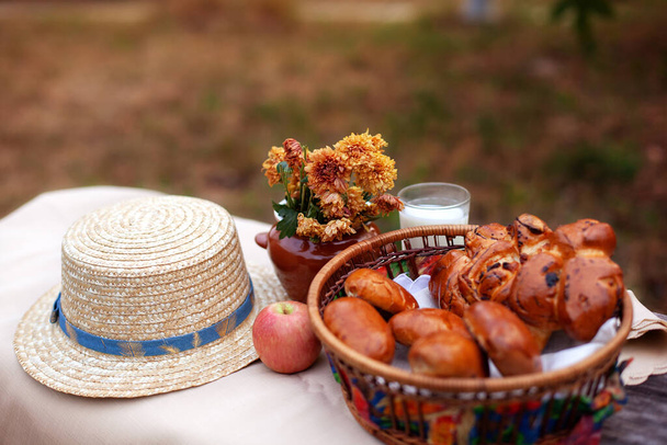 古い素朴なテーブルの上に屋外の夏のピクニック。秋の公園では、パン、パン、ミルクのガラス、木製のテーブルの上の花の花束と美しい素朴なピクニック組成。健康食品のコンセプト.  - 写真・画像
