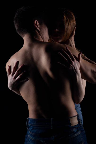 Vášnivý pár: žena s lehkými vlasy a pohledný neoholený muž něžně objímat navzájem v nízkém světle - Fotografie, Obrázek