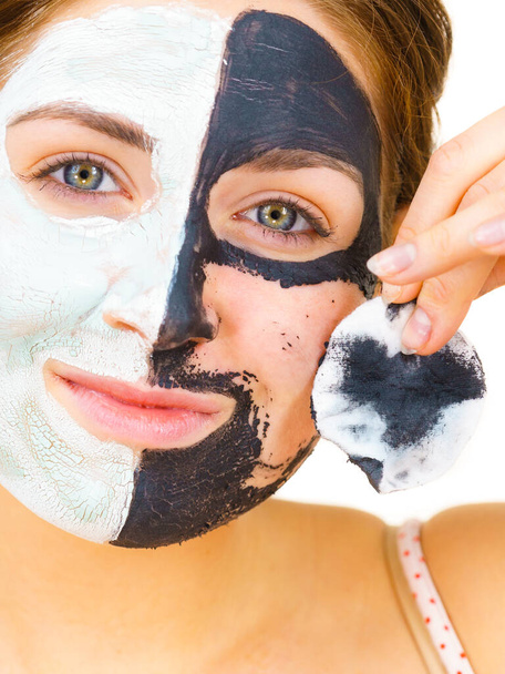 Woman with clay carbo black mask on one half face and white mud on second half. Girl removing cosmetic scrab with cotton swab. Female taking care of oily complexion. Skincare. - Фото, зображення