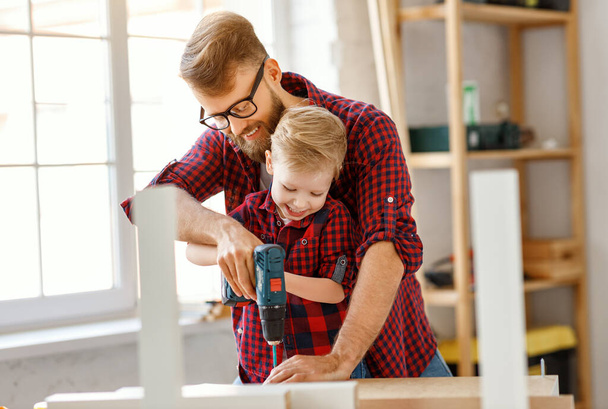 Muchacho emocionado y padre joven en camisas similares que sostienen taladro juntos mientras se trabaja con madera en los estudios de artesanía moderna
 - Foto, imagen