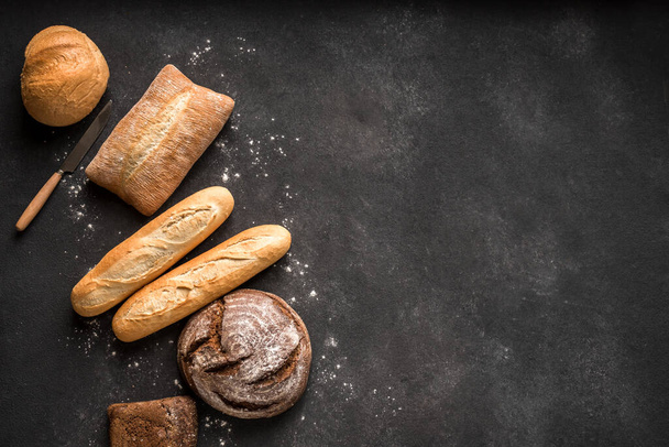 Fris brood op zwarte achtergrond, bovenaanzicht, kopieerruimte. Zelfgebakken vers gebakken verschillende broodjes tarwe en roggebrood van dichtbij. - Foto, afbeelding