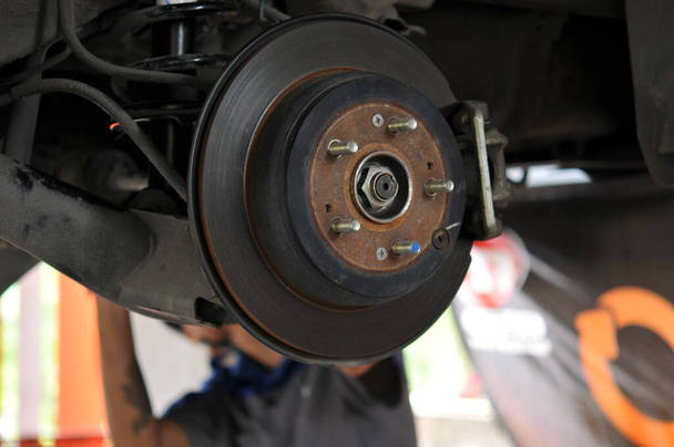 Mecánico automático en proceso de reemplazo de neumáticos nuevos, reparación de frenos de coche en el garaje, frenos en un coche con rueda extraída, pieza de freno de coche en el garaje, disco de freno de coche sin ruedas de primer plano
  - Foto, Imagen
