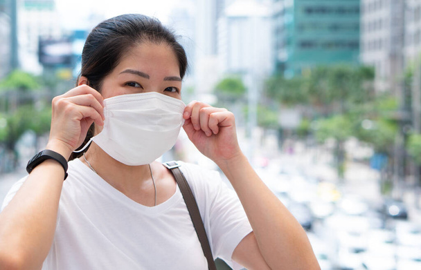 mladá asijská žena s obličejovou maskou pomocí smartphonu a procházky ve městě během covid-19 nebo coronavirus vypuknutí. sociální distancování a nový koncept normálního životního stylu - Fotografie, Obrázek