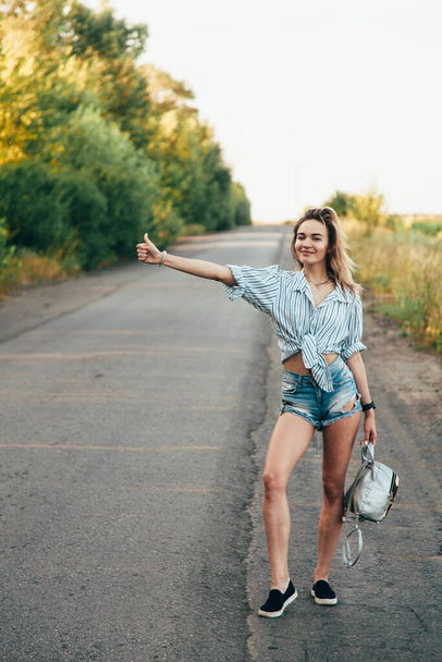 Beautiful girl hitchhiking on the track in a mans shirt - Fotoğraf, Görsel