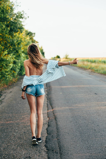 Beautiful girl hitchhiking on the track in a mans shirt - Foto, afbeelding