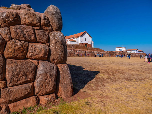 Antico muro Inca fatto di blocchi di pietra con la chiesa coloniale dei conquistatori spagnoli come sfondo nella piazza principale, villaggio di Chinchero, Perù - Foto, immagini