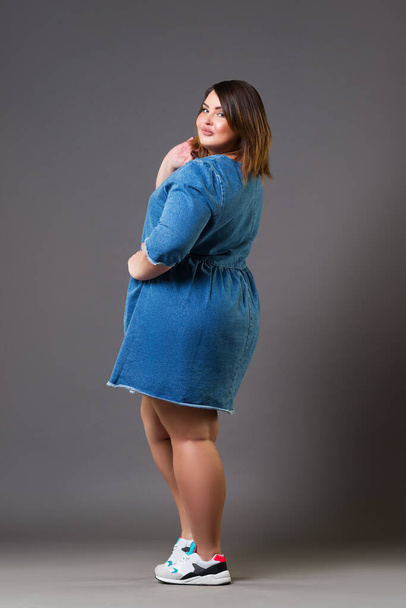 Plus size fashion model in a denim dress, fat woman on gray background, body positive concept - Photo, Image