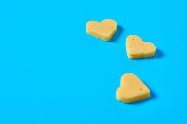 Three pieces of cheese in form of heart lies on blue desk on kitchen. Concept of Valentine's Day. Space for text - Foto, Imagem