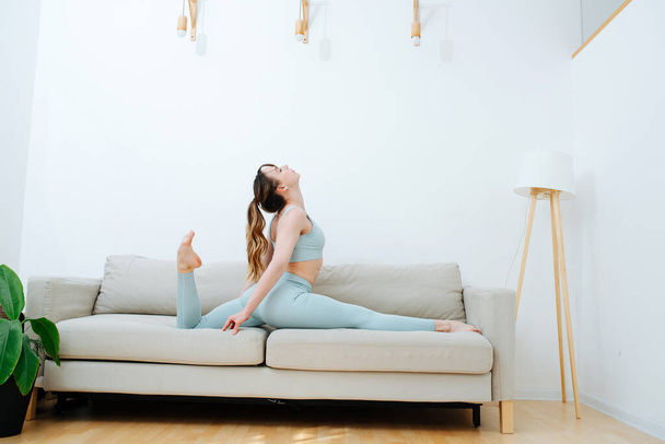Ejercicios de entrenamiento en casa, una chica caer en las divisiones en el sofá, haciendo estiramiento diario
 - Foto, Imagen