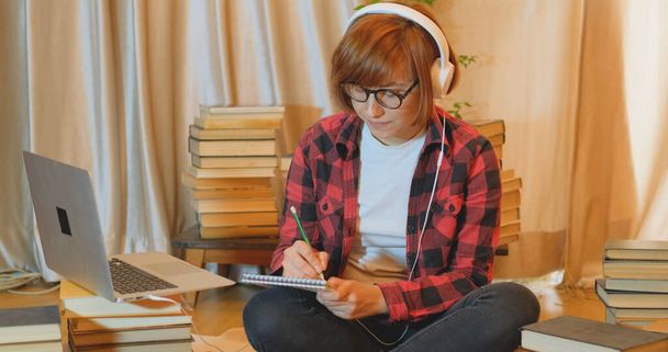 Evde birçok kitap ve dizüstü bilgisayarla okuyan genç bir kız öğrenci. - Fotoğraf, Görsel