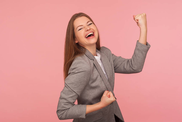 Yes I did it! Portrait of successful enthusiastic young woman in business suit screaming for joy with raised fists, celebrating victory and laughing. indoor studio shot isolated on pink background - Foto, immagini