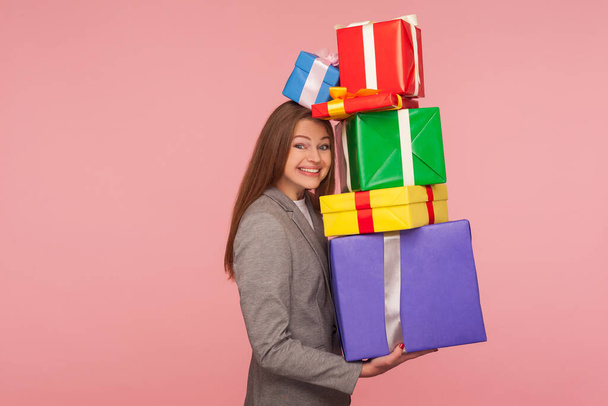 So many presents! Portrait of happy joyful woman holding lot of wrapped boxes and smiling excitedly at camera, enjoying mount of bonuses and gifts. indoor studio shot isolated on pink background - Foto, Imagem
