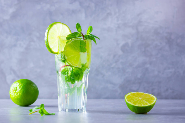 Mojito cocktail with lime and mint in tall glass. Fresh mojito in glass on a gray background. Refreshing mint cocktail with lime. Infused water. Copy space - Foto, Imagem