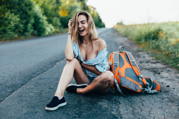 Beautiful girl hitchhiking on the track in a mans shirt - Foto, afbeelding