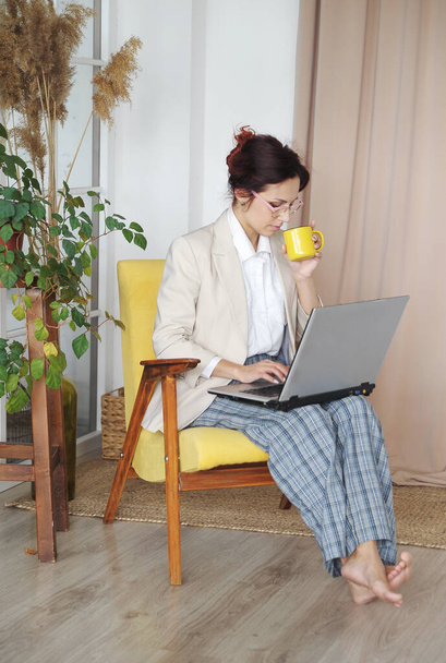 Γυναίκα με φορητό υπολογιστή λειτουργεί από το σπίτι. Γυναίκα με σακάκι γραφείου και παντελόνι στο σπίτι επικοινωνεί με τους εργαζόμενους. Έννοια απομακρυσμένης εργασίας. - Φωτογραφία, εικόνα