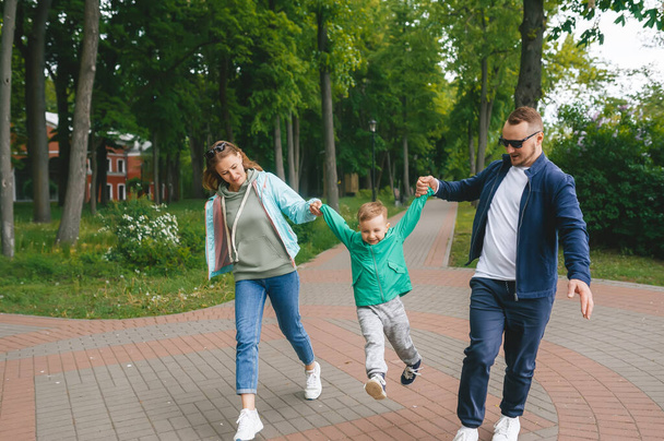 Family walking down theroad outside in the city park. Family is holding each other hands. The little son is between father and mother. - Valokuva, kuva
