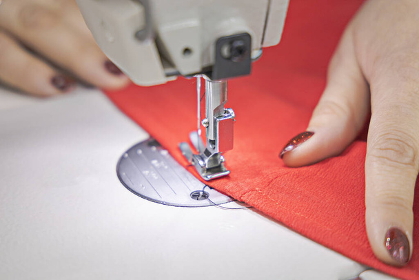 De meester naait op een naaimachine. De meester naait rode stof op een naaimachine. Sluitingsdatum - Foto, afbeelding