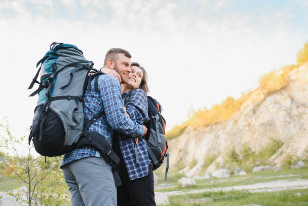 暖かい晴れた夜に美しいロッキートレイルのバックパックでハイキングする若い幸せな旅行者のカップル。家族旅行とアドベンチャーのコンセプト. - 写真・画像
