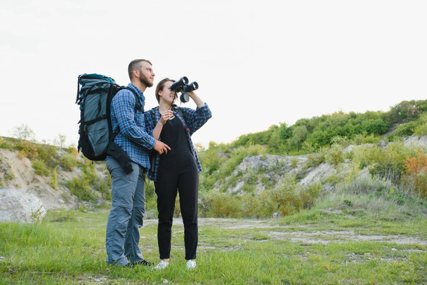 Couple enjoying beautiful views on the mountains, while traveling with backpacks in the mountains during the summer vacations - Фото, зображення