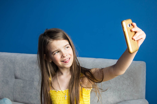 girl takes a selfie on her phone in a room with blue walls - Фото, изображение